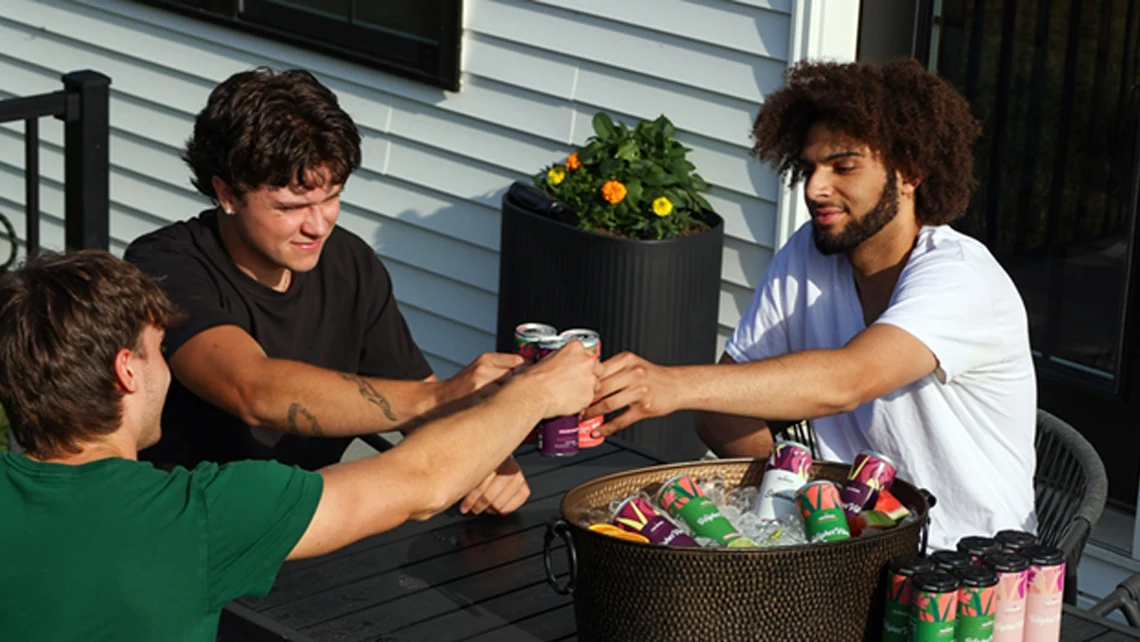 Three friends on a porch toasting with Wunder weed drinks above a basket of THC cans.