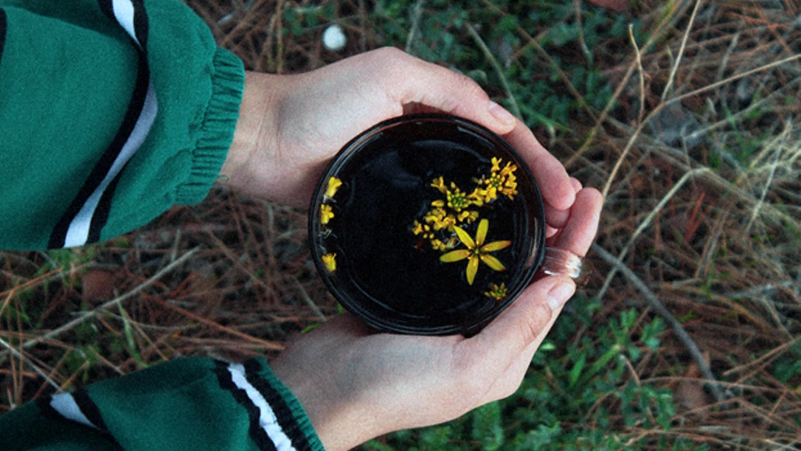 Hands holding a glass of beverage with floating yellow flowers