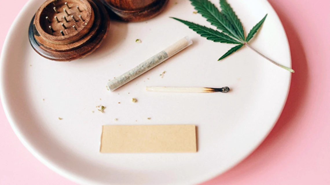 Round plate with a cannabis leaf, match, rolled joint, and weed grinder filled with crushed cannabis