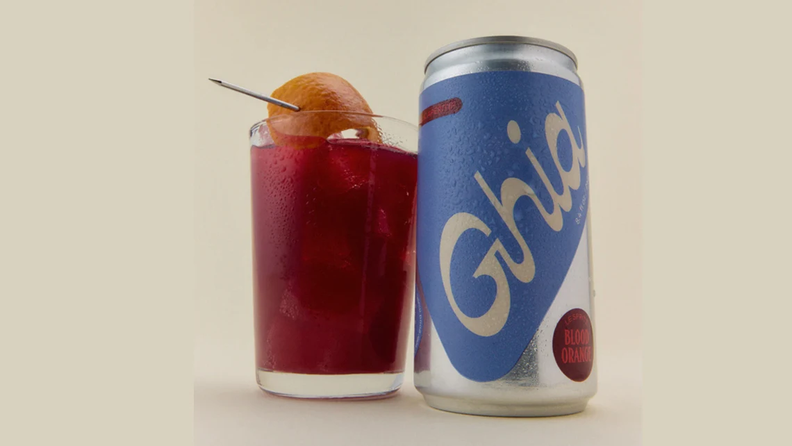a can of Ghia Apéritif Le Spritz Blood Orange beside a glass of the red apéritif with an orange rind
