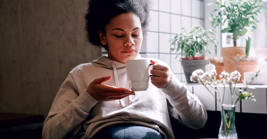 black woman sitting back as she looks into her mug, contemplating an alcohol-free lifestyle