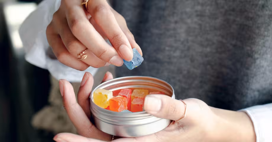 close-up photo of a woman’s hand picking a single gummy from a tin can of THC gummies she’s holding