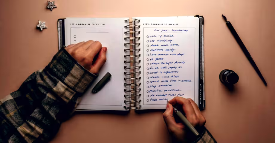 hands of a girl wearing a plaid sweater writing down New Year’s resolutions in a notebook