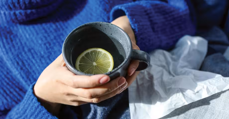 hands of an alcohol-free woman wearing a blue sweater holding a cup of water with a lemon slice