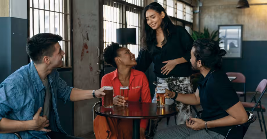 woman approaching her 3 friends who are seated around a circular table