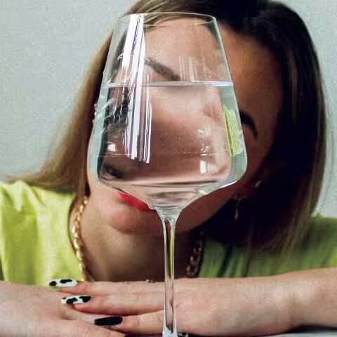 woman in a yellow shirt staring at a wine glass halfway full with water