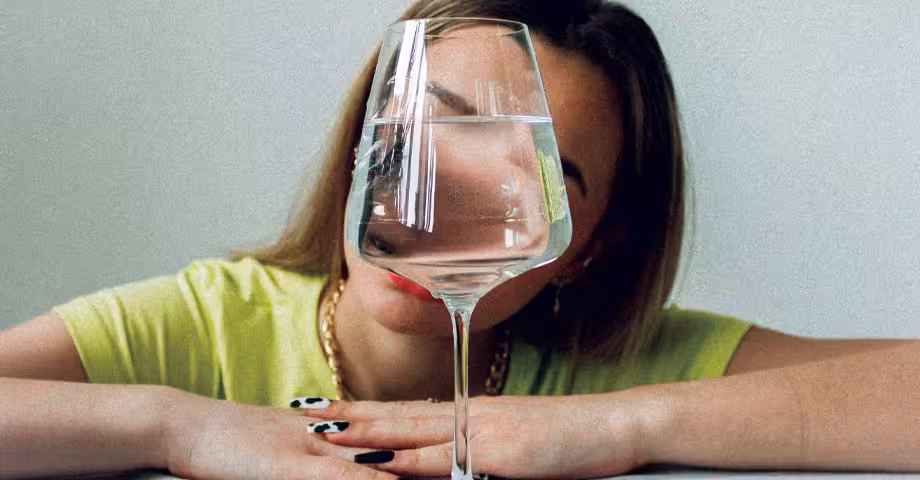 woman in a yellow shirt staring at a wine glass halfway full with water