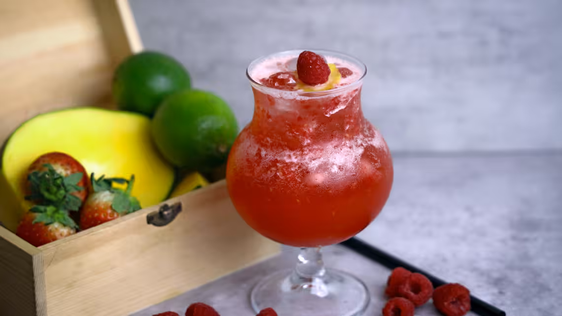 a glass of fizzy raspberry lemonade garnished and surrounded with raspberries beside a box of fruits