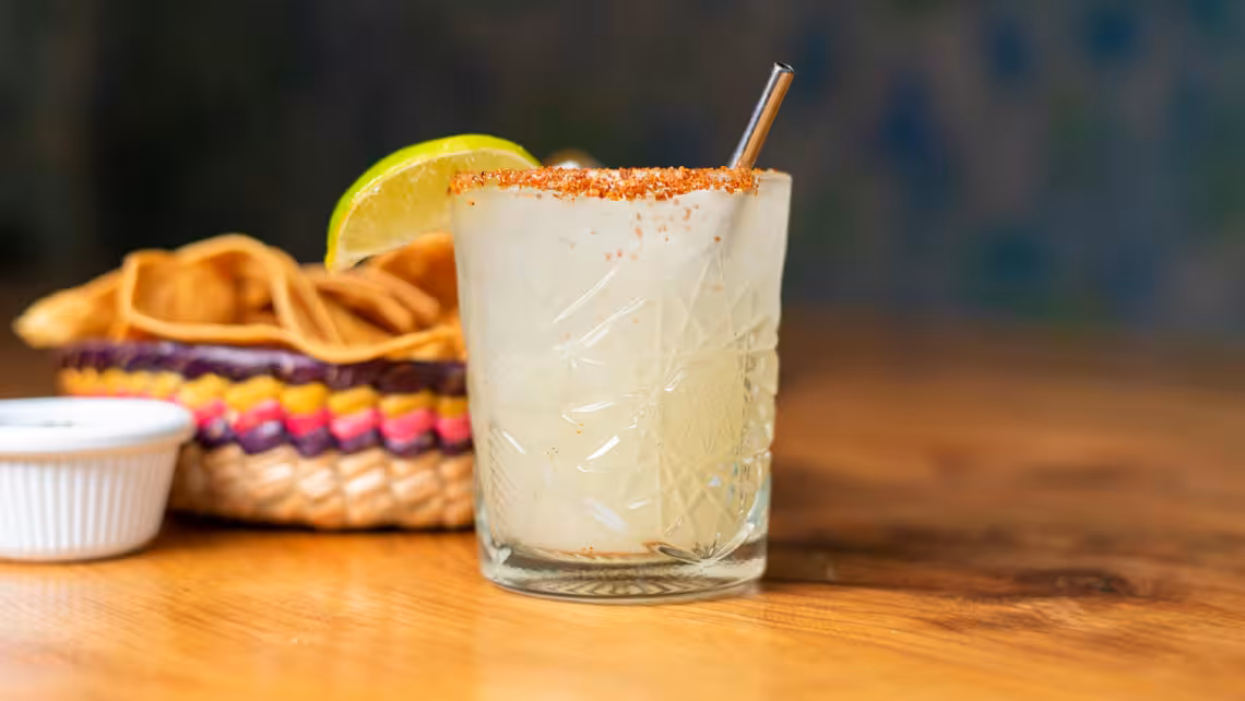 glass of NA spicy jalapeño margarita garnished with a lime wedge with chips and dip beside it